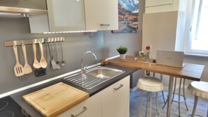 A modern kitchen with a built-in stove, a sink, and a wooden countertop. There are bar stools and a laptop on the counter. - Charming House in Old Town Desenzano (Desenzano del Garda)