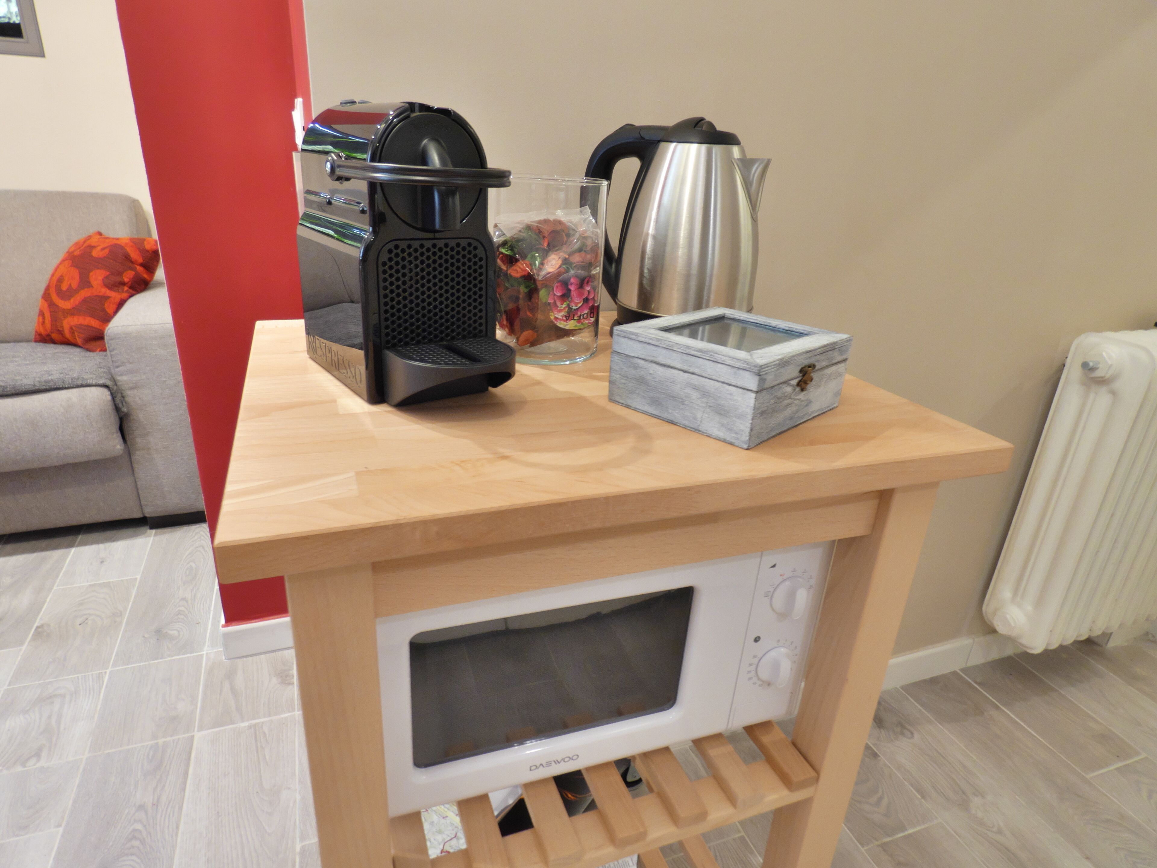 A compact kitchen setup with a wooden countertop, a coffee maker, a kettle, a microwave, and a small storage box.