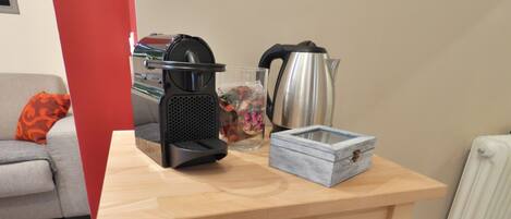 A compact kitchen setup with a wooden countertop, a coffee maker, a kettle, a microwave, and a small storage box.