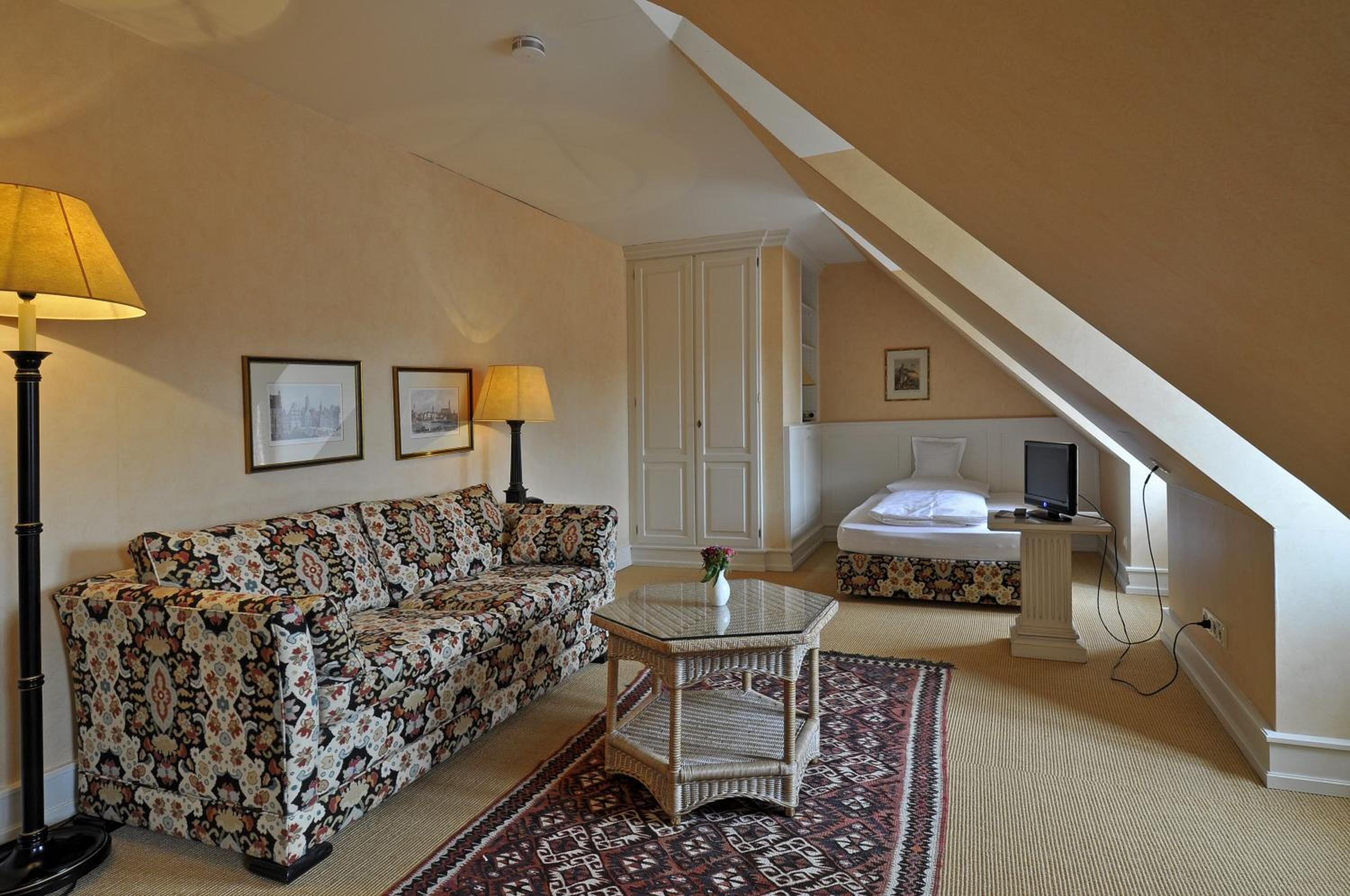 A cozy room with a patterned sofa, a small glass table, and a bed with a TV.