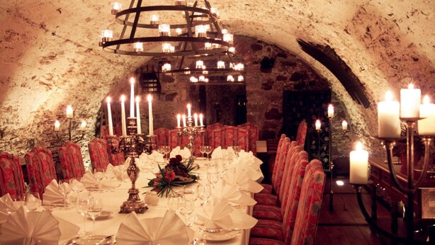 A dining area with a long table set for a meal, surrounded by red upholstered chairs, and a chandelier hanging from the ceiling. - Hotel Herrenhaus von Löw (Bad Nauheim)