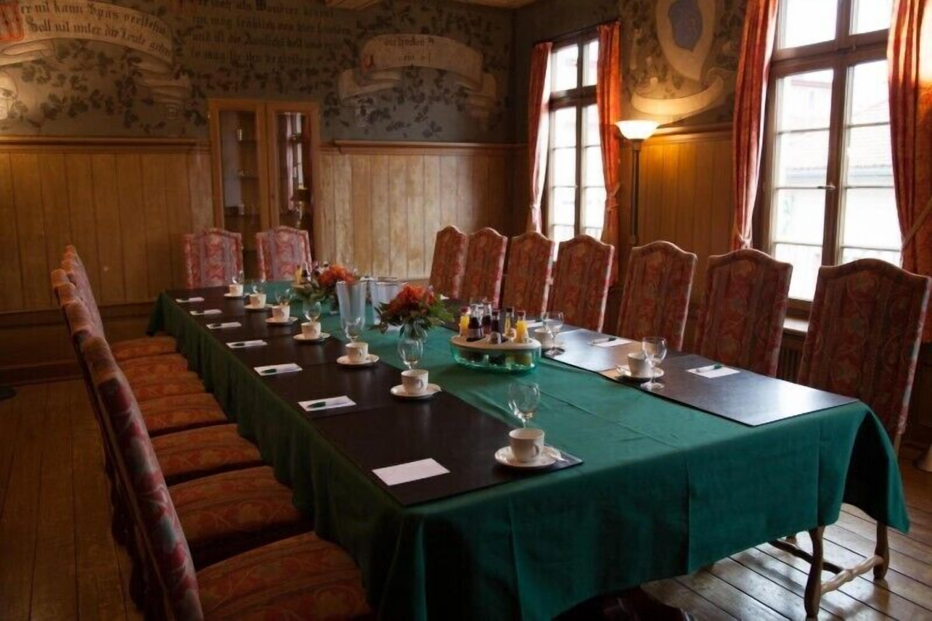A conference room with a long table set for a meeting, surrounded by upholstered chairs.