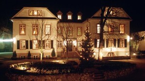 A large, two-story building with a symmetrical facade, multiple windows, and a central staircase leading to the entrance. - Hotel Herrenhaus von Löw (Bad Nauheim)