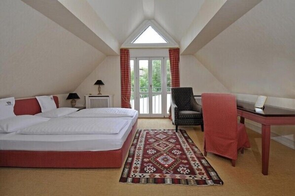 A bedroom with a bed, a chair, a table, and a window with curtains.