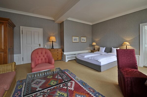 Una habitación de hotel con cama, dos sillones, un sofá, una cómoda y una mesita de noche.
