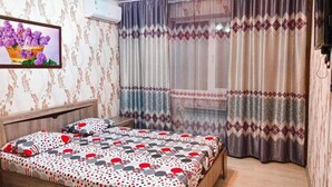 Ein Schlafzimmer mit Bett, Vorhängen, einem an der Wand befestigten Fernseher und einem gerahmten Bild.