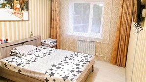 Ein Schlafzimmer mit Bett, Fenster, Vorhängen, Heizkörper und einem Bild an der Wand.