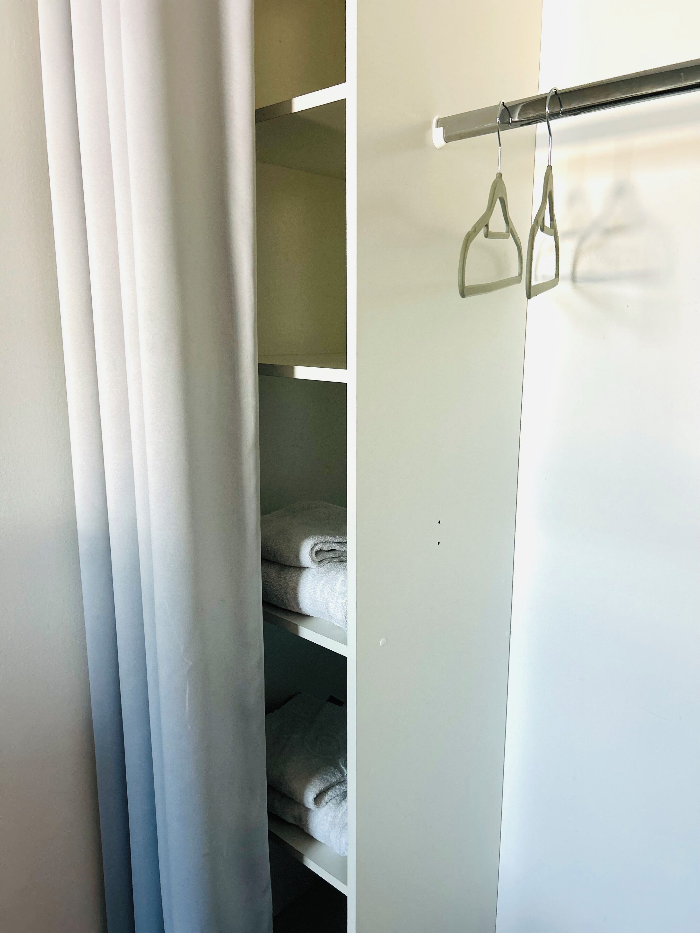 Un placard contenant des serviettes pliées avec soin et une tringle en métal avec des cintres.