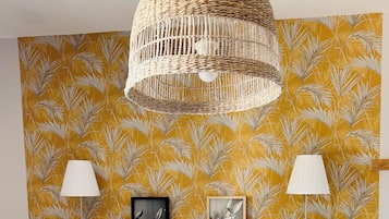 A bedroom with a white bed, a woven headboard, two wall-mounted lamps, and two framed pictures.