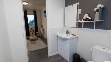 Ein modernes Badezimmer mit Waschbecken, Spiegel und Toilette. Im angrenzenden Raum steht ein kleiner runder Tisch mit einem Blumenstrauß.