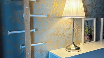 A room with a wall-mounted rack holding white cylindrical objects, a table with a lamp, and framed pictures.