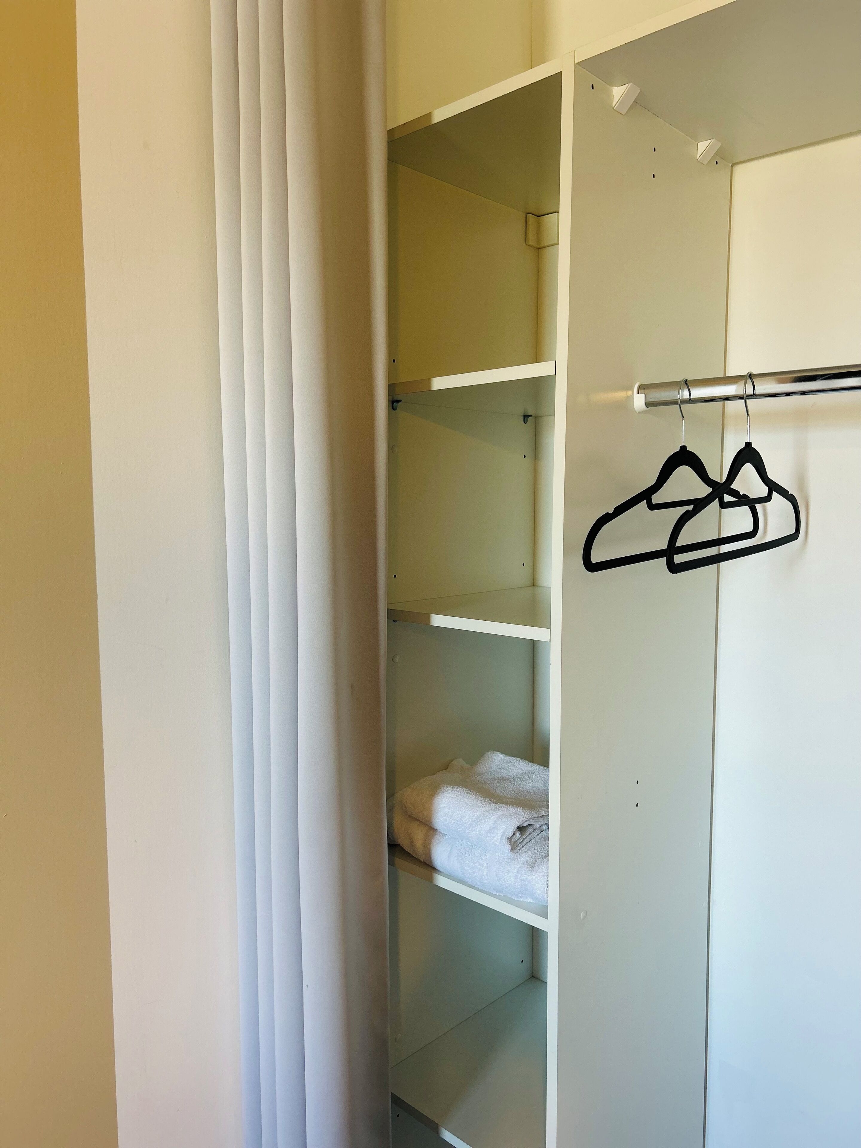 Ein weißer Kleiderschrank mit mehreren Regalen, einer Kleiderstange und einem gefalteten Handtuch auf der untersten Ablagefläche.