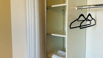 Ein weißer Kleiderschrank mit mehreren Regalen, einer Kleiderstange und einem gefalteten Handtuch auf der untersten Ablagefläche.