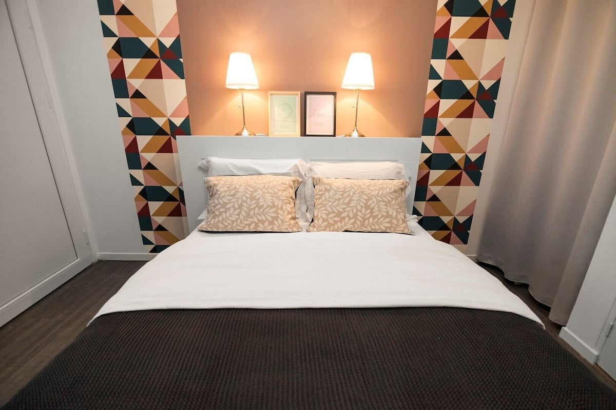Une chambre d’hôtel avec un lit, deux lampes de chevet, une tête de lit et des murs ornés de motifs géométriques.