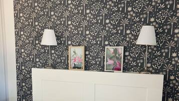 A bedroom with a white bed, a headboard with two wall-mounted lamps, and a floral-patterned wallpaper.