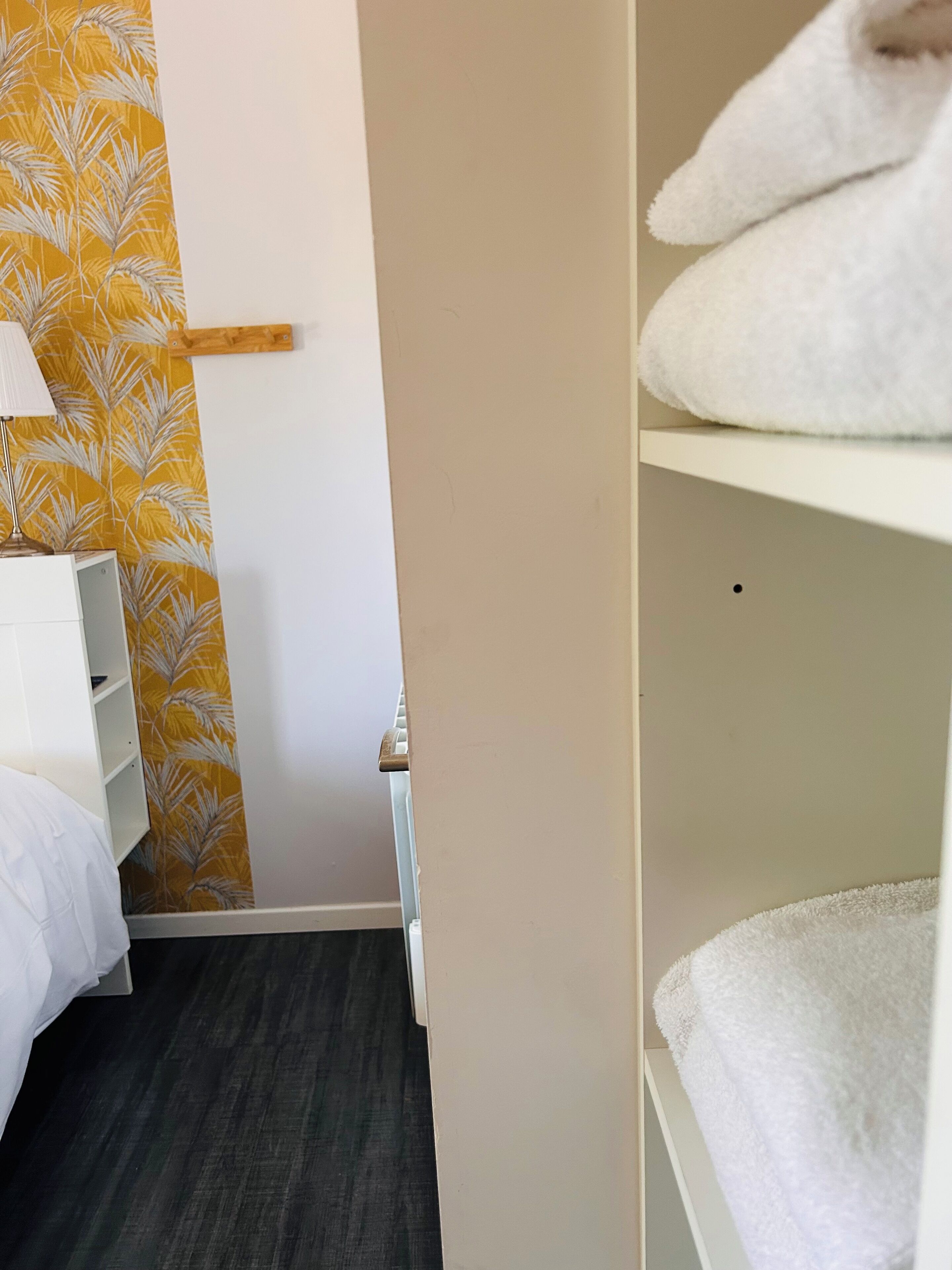 Una habitación de hotel con cama, mesita de noche, lámpara y armario con toallas.