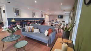Een moderne woonkamer met een grijze bank, een glazen salontafel en een eethoek met witte stoelen.
