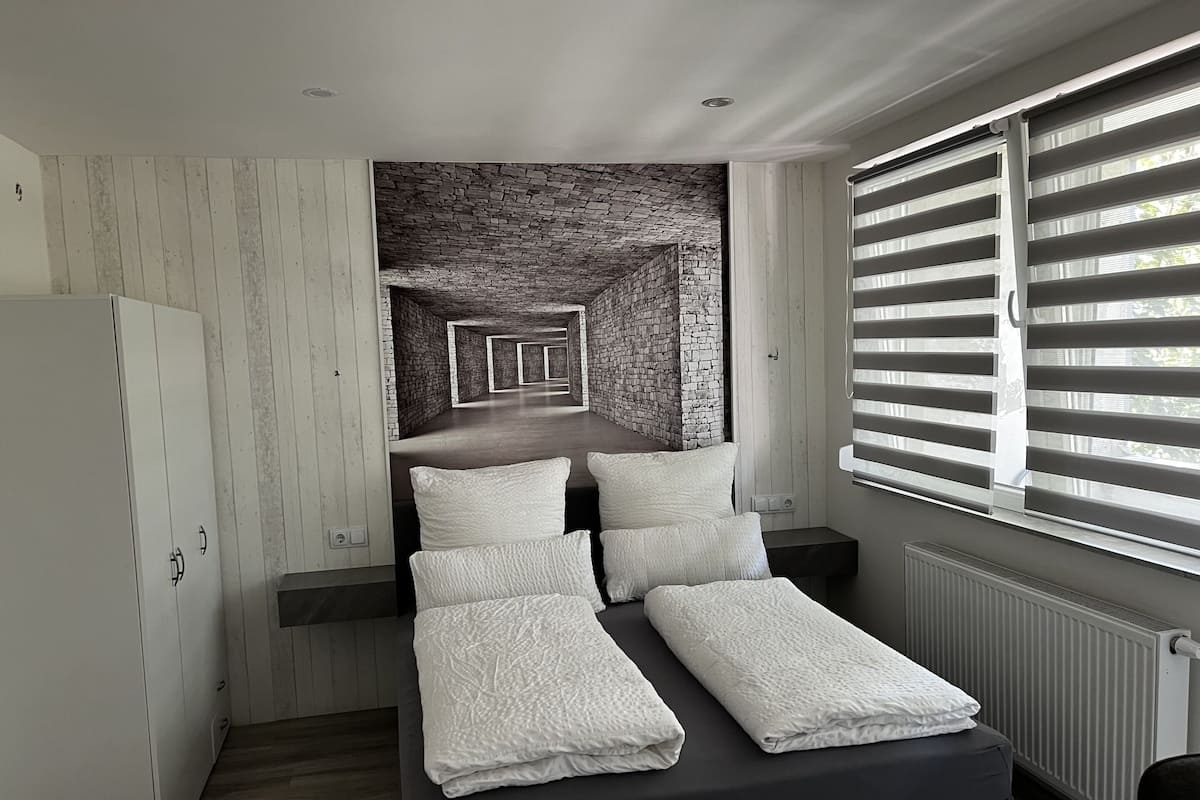 Een slaapkamer met een bed, een kledingkast, een radiator en een raam met jaloezieën.