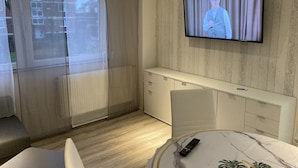 Une chambre d’hôtel moderne dotée d’un grand téléviseur fixé au mur, d’une porte-fenêtre coulissante donnant sur un balcon, d’une console blanche et d’une table au motif de marbre.