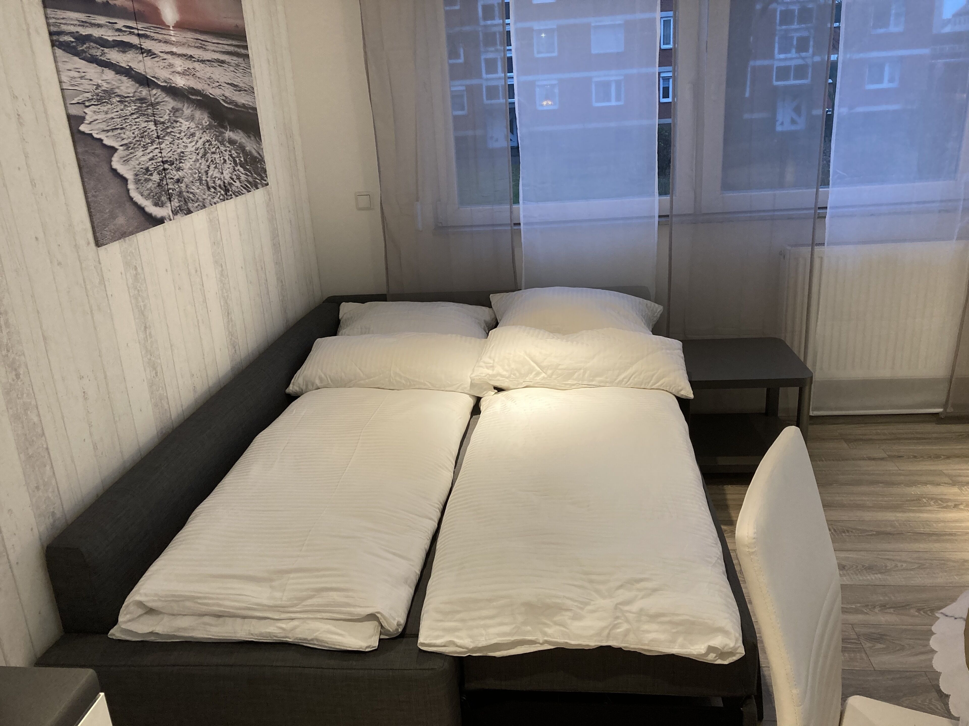 A small, neatly arranged room with a bed, a bench, and a chair.