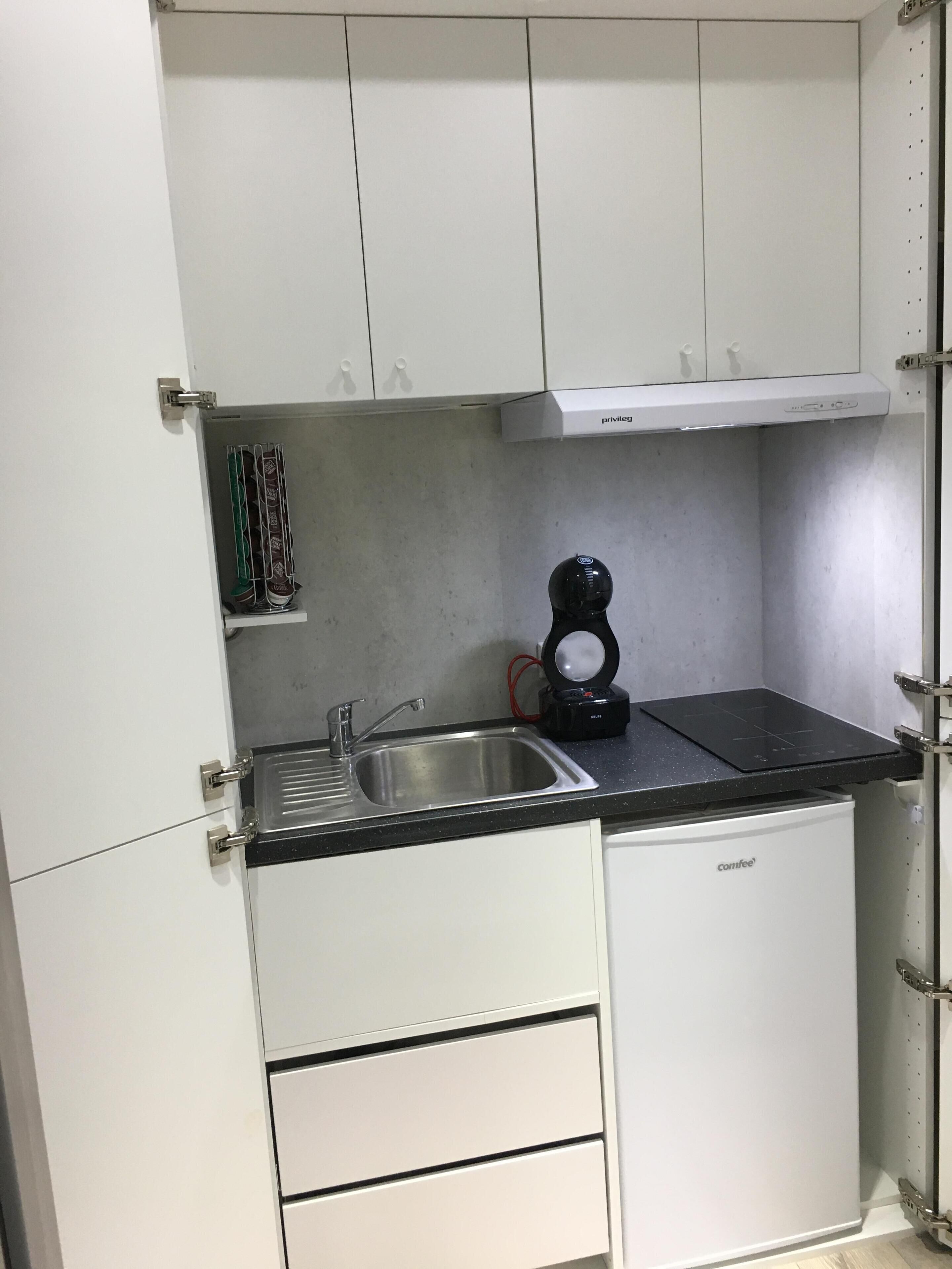 A compact kitchen with white cabinets, a built-in sink, and a coffee maker.