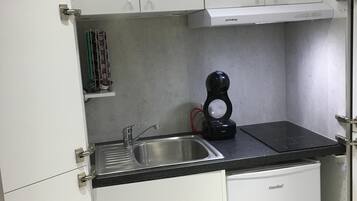 A compact kitchen with white cabinets, a built-in sink, and a coffee maker.