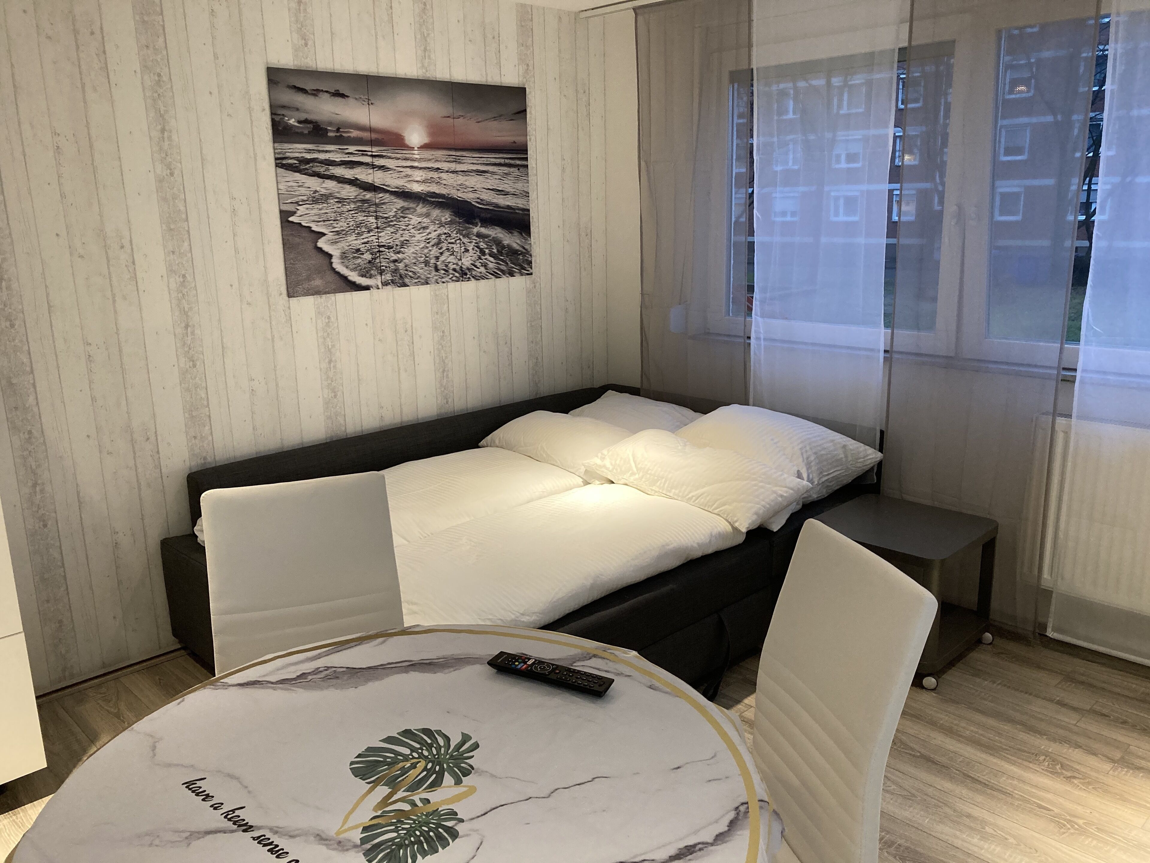 Ein gemütliches Schlafzimmer mit Bett, Nachttischen, einem kleinen Tisch mit Fernbedienung und einem an der Wand hängenden Bild.