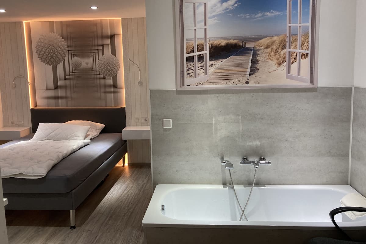 Een moderne slaapkamer met een bed, een groot raam met uitzicht op het strand en een bad.