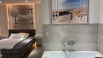 Ein modernes Schlafzimmer mit einem Bett, einem großen Fenster mit Blick auf den Strand und einer Badewanne.