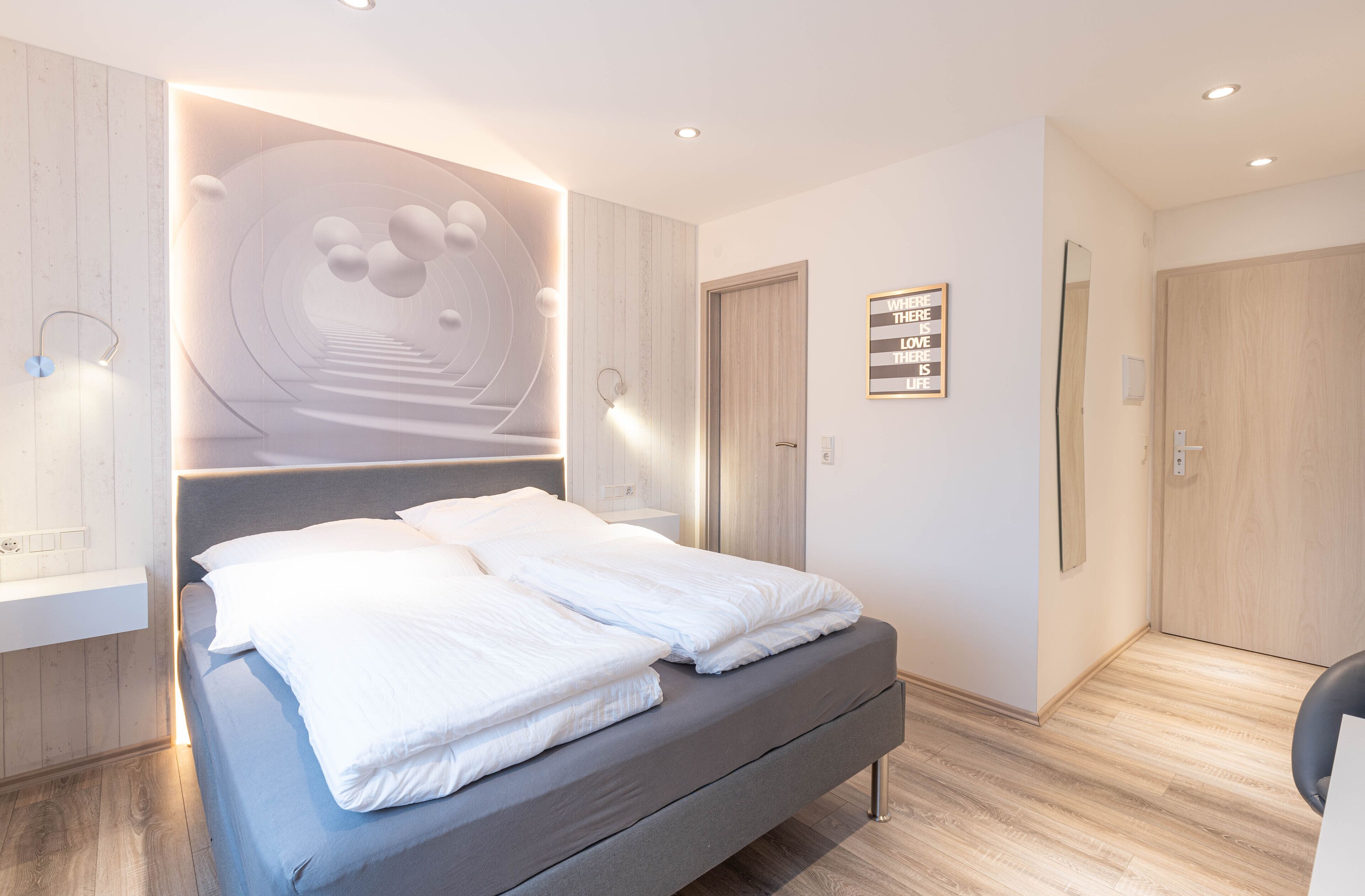 Een moderne slaapkamer met een bed, een wandlamp en een deur.