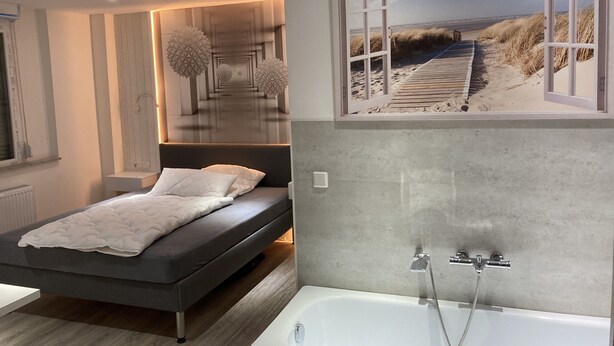 Une chambre moderne avec un lit, une grande fenêtre donnant sur la plage et une salle de bain avec une baignoire.