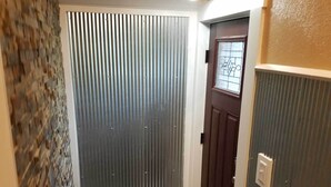 Een smalle trap met een houten leuning, een vloermat met patroon aan de onderkant, een metalen deur met raam, en een gestructureerde wand aan één kant.