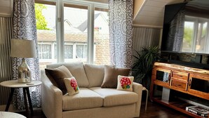 Een gezellige woonkamer met een beige bank, decoratieve gordijnen, een houten tv-meubel en een groot raam.