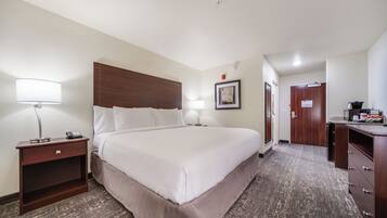 Camera d'albergo con un letto grande, comodini con lampade, una testiera in legno, un quadro incorniciato appeso al muro, una scrivania con un computer e una porta che conduce a un'altra stanza.