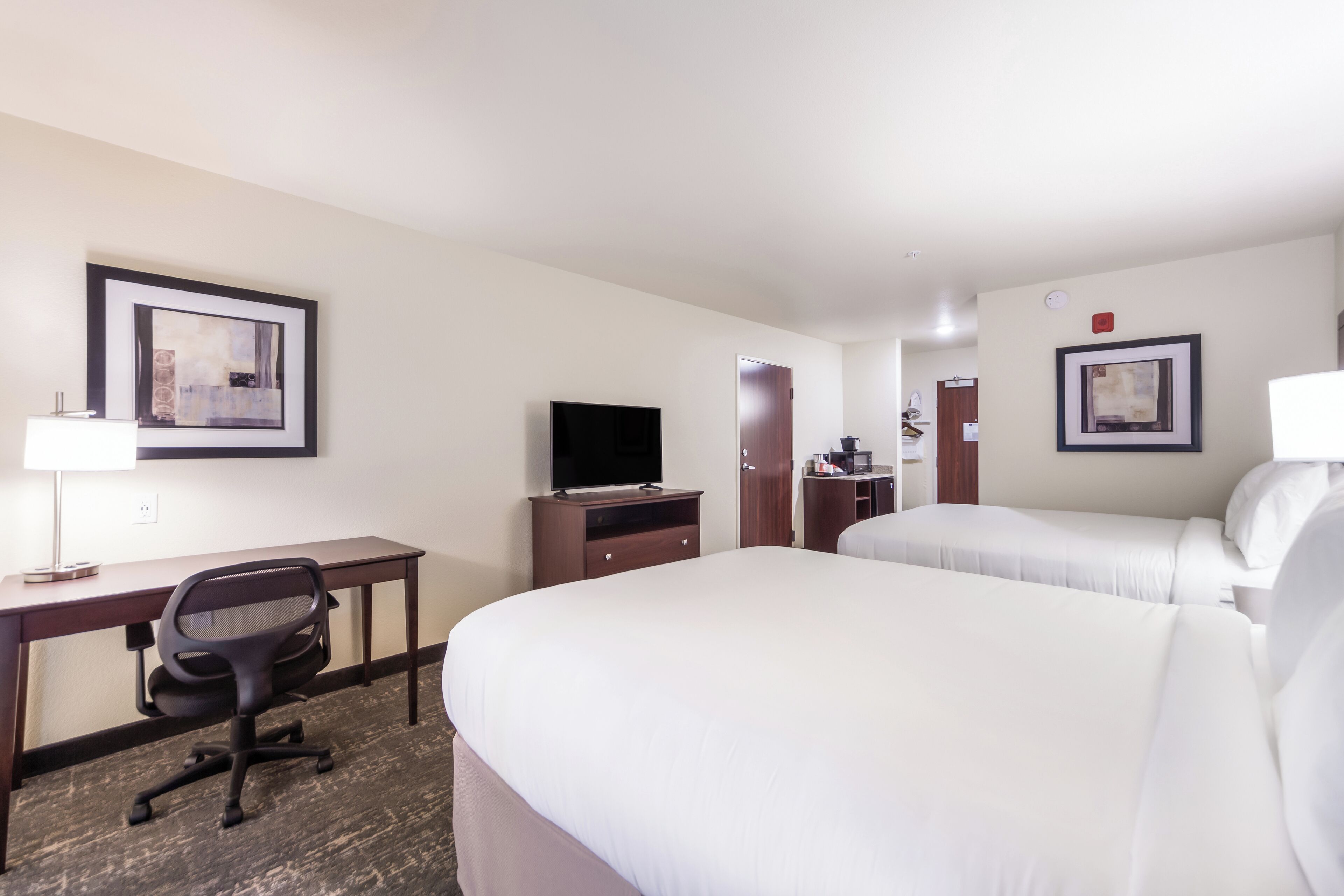 A hotel room with a desk, two beds, a television, and framed artwork on the walls.