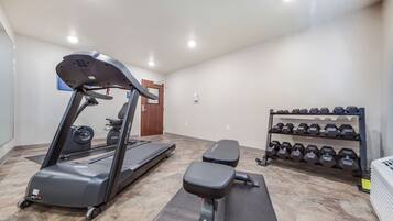 Un gimnasio con cintas de correr, una banca y una estantería con mancuernas.