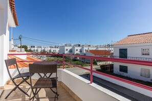 Ein Balkon mit Blick auf benachbarte Gebäude, einem roten Geländer und zwei Korbstühlen.