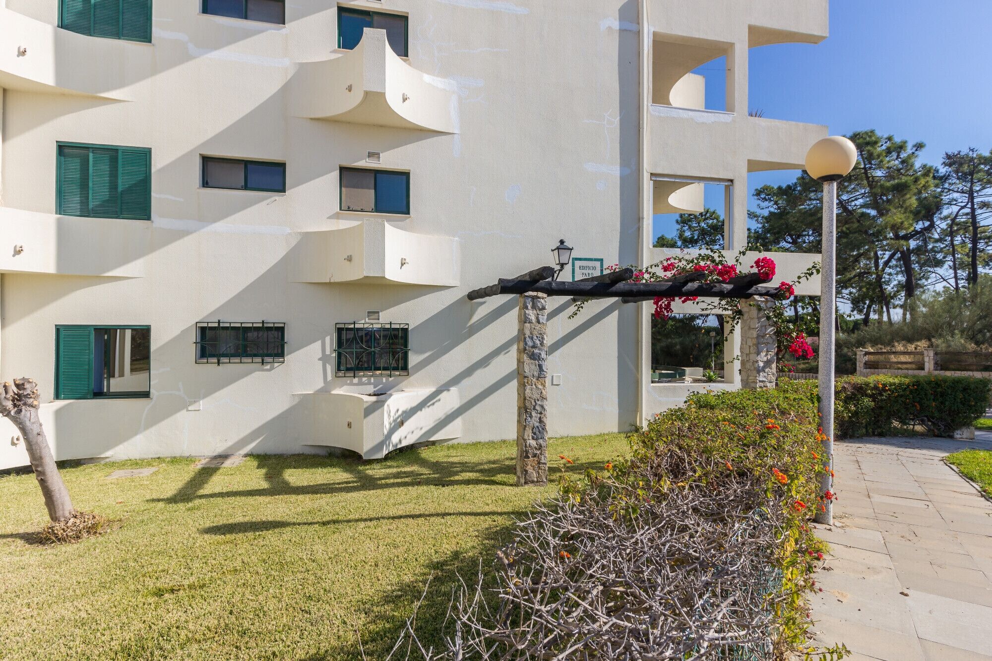 Um edifício moderno com varandas, uma pérgula florida e um gramado bem cuidado.