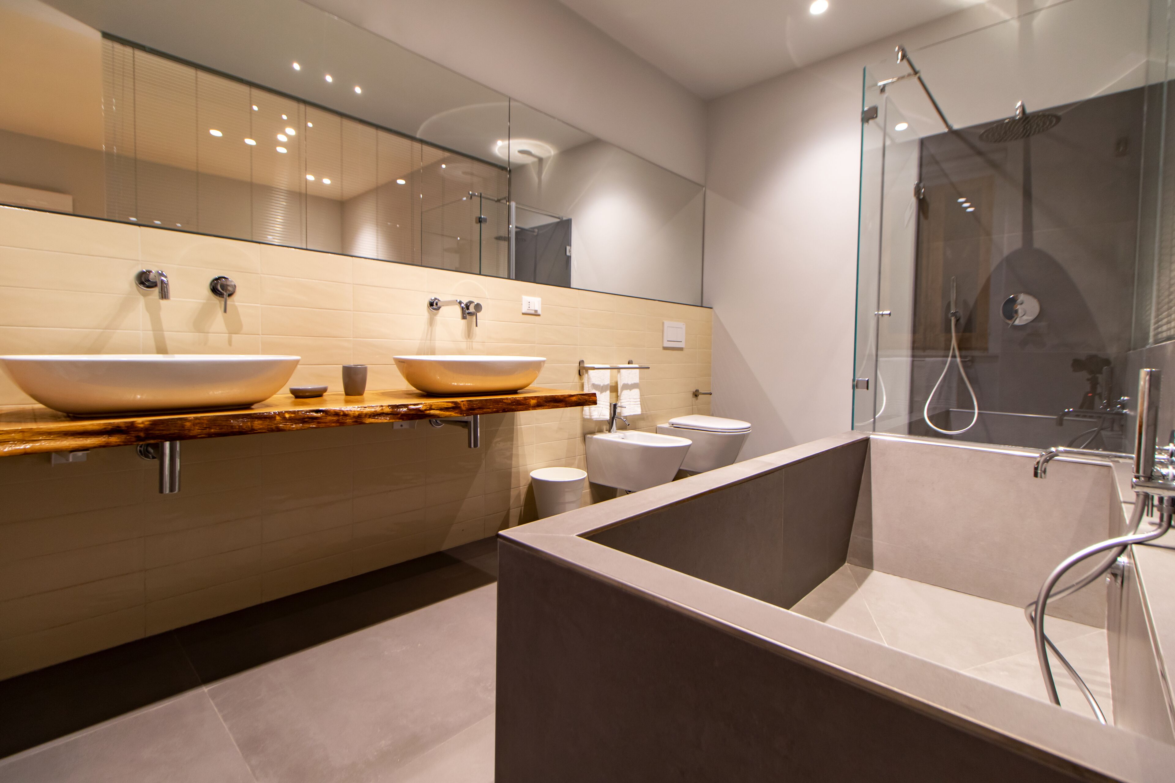 Une salle de bain moderne dotée d’une grande baignoire, de deux lavabos et d’une douche séparée par une paroi en verre.
