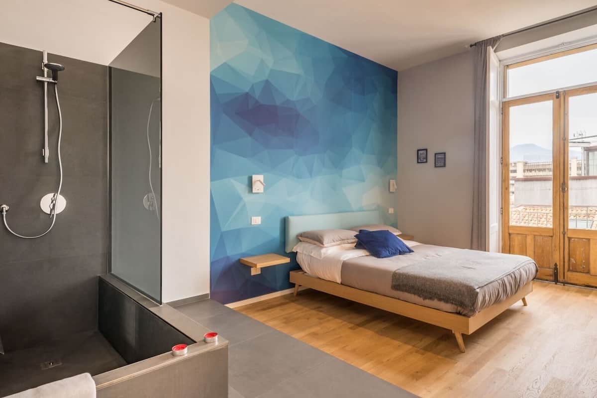 A modern bedroom with a bed, a shower area, and a geometric wall design.