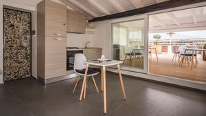 A modern kitchen with wooden cabinets, a built-in oven, and a dining area with a table and chairs. - Terrazza Sangiuliano (Catania)