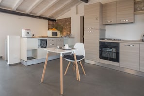 A modern kitchen with a built-in oven, a microwave, and a coffee machine. There is a small dining area with a table and two chairs. - Terrazza Sangiuliano (Catania)