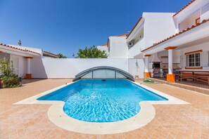 Ein Schwimmbecken mit einer gewölbten Glasumrandung, umgeben von einer gefliesten Terrasse und weißen Wänden mit orangen Akzenten.