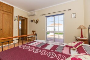 Ein Schlafzimmer mit Bett, Stuhl, Tisch, Klimaanlage, Fenster und Tür.