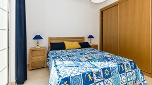 Un dormitorio con una cama, dos mesitas de noche, un armario de madera y una ventana con cortinas.