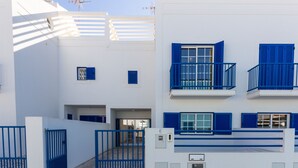 Un edificio moderno con fachada blanca y detalles azules, que cuenta con balcones y una entrada protegida por una reja.