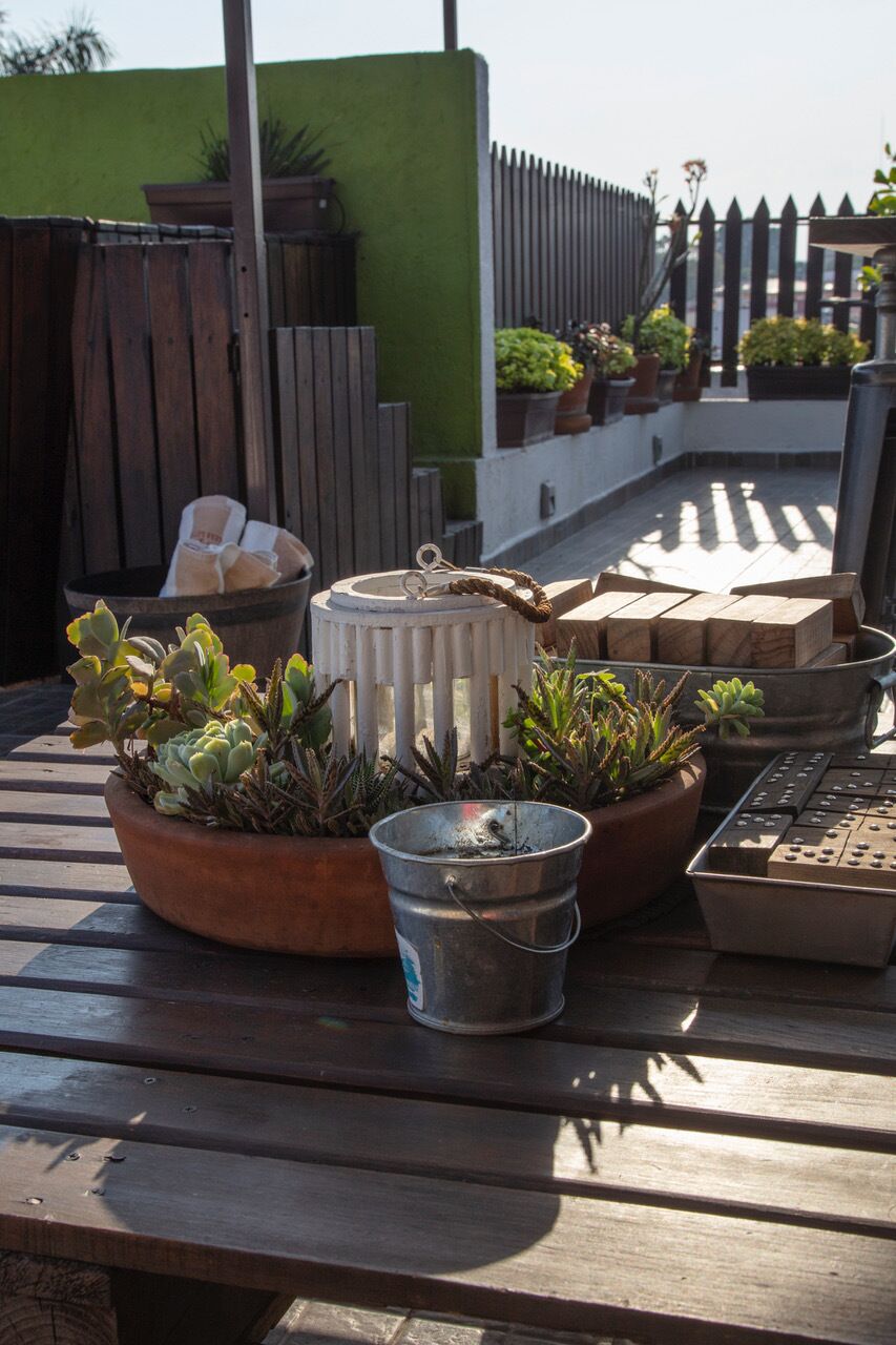 A rooftop patio with potted plants, a metal bucket, and a white lantern.