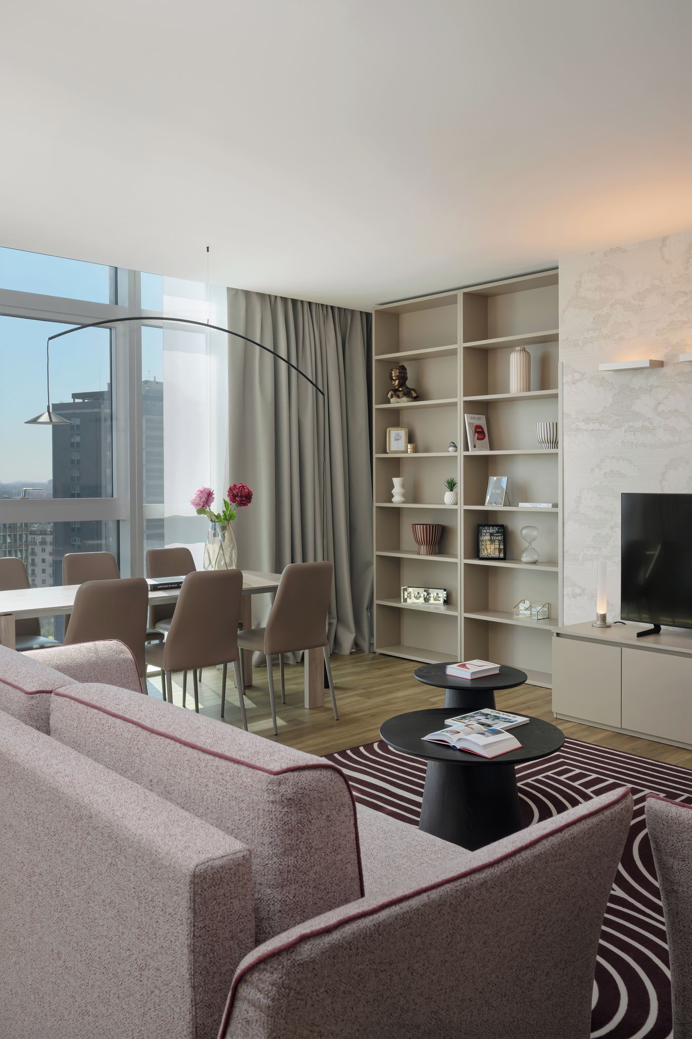 A modern living room with a sofa, chairs, a coffee table, a bookshelf, and a television.