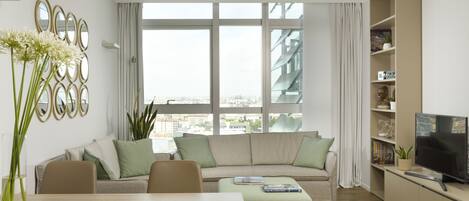 Een moderne woonkamer met een bank, eettafel, stoelen, een televisie en een boekenkast.