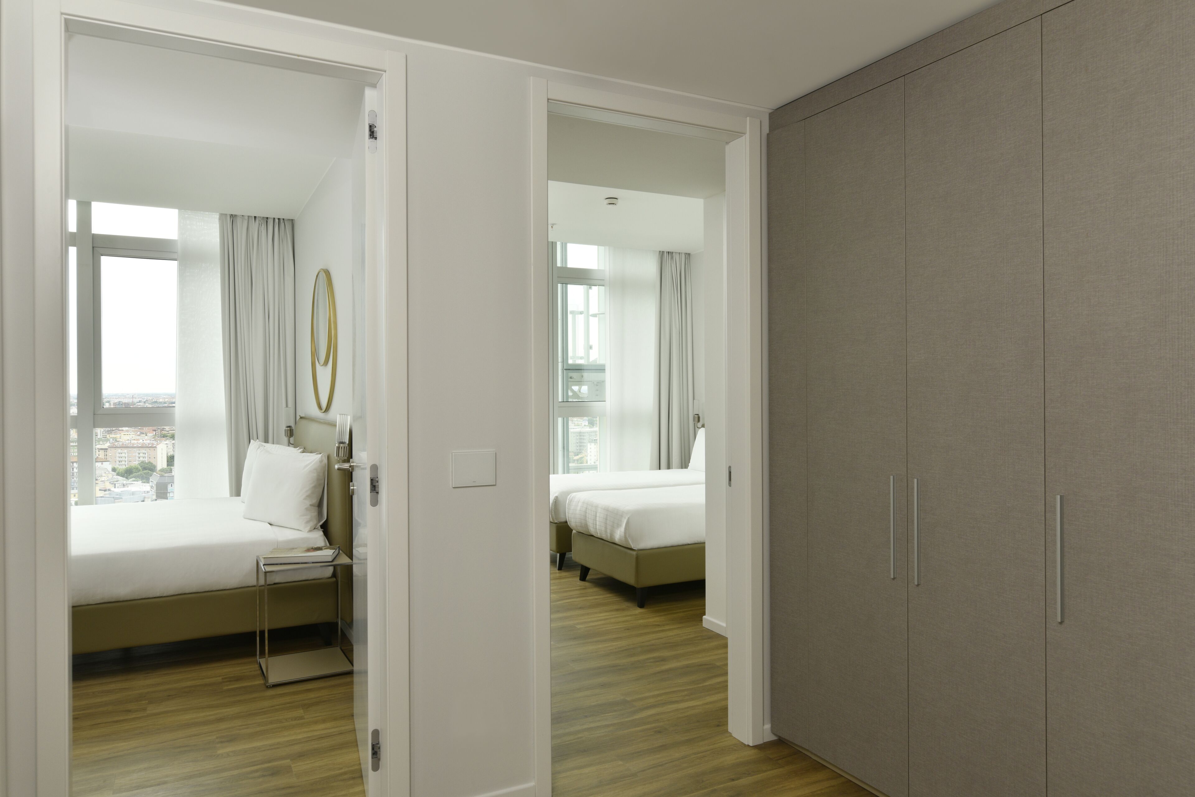 A hotel room with two beds, a wardrobe, and a view of the city.